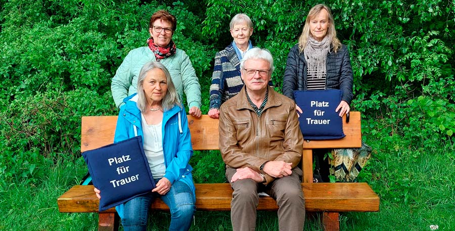 Personen sitzen mit Kissen auf der Trauerbank